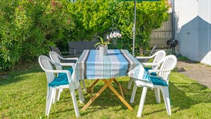 En uteplats med ett bord och stolar, en grill och ett grönt parasoll.