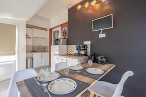 A dining area with a table set for four, a kitchen with modern appliances, and a flat-screen TV mounted on the wall.