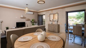 A modern living room with a sofa, TV, dining table, and a view of the outdoors. - Holiday Home Timos Villa with Mountain View, Wi-Fi and Air Conditioning (Zakynthos)