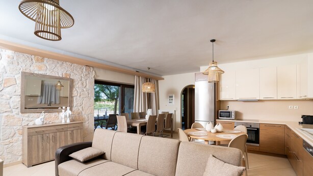 A modern living room with a sofa, dining table, and kitchen area with cabinets and appliances. - Holiday Home Timos Villa with Mountain View, Wi-Fi and Air Conditioning (Zakynthos)