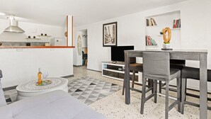 Una cocina moderna con armarios blancos, un comedor con mesa y sillas, y una sala de estar con sofá y televisor.