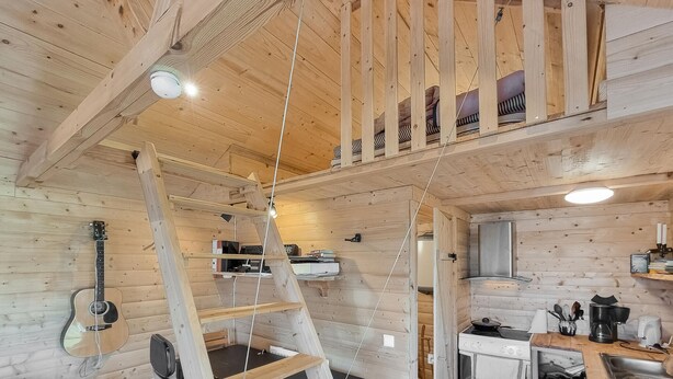 Un interno accogliente in legno con una camera da letto soppalcata, angolo cottura e una scala che conduce al soppalco.
