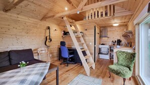 Accogliente interno di una baita con arredamento in legno, un divano, una scrivania, una sedia, una scala e un angolo cucina.