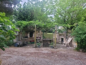 A rustic outdoor area with a stone structure, a wooden table, a bench, and potted plants.