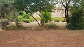 A dry, grassy field with scattered trees and a building with a tiled roof in the background. - Holiday Home 'Pey Sud' with Mountain View, Private Terrace and Wi-Fi (Sistels)