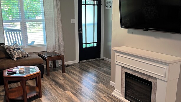 A living room with a fireplace, a television mounted on the wall, and a door with a window. - Cozy modern farmhouse w/ garage- Only 5 miles to Lake Cumberland! (Monticello)