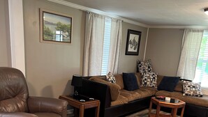 A living room with a leather armchair, a sofa with patterned cushions, a coffee table, and a wooden floor. - Cozy modern farmhouse w/ garage- Only 5 miles to Lake Cumberland! (Monticello)