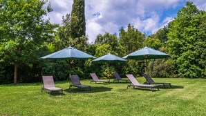 Un jardín con cuatro sillas de descanso y tres sombrillas.