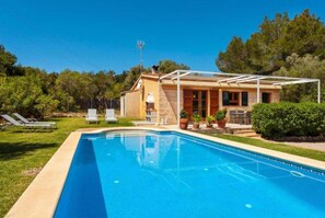 Une piscine avec des chaises longues, un patio couvert et une maison à la façade en pierre.