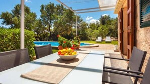 An outdoor patio with a table, chairs, a bowl of fruit, a pool, and a garden. - Country House 'Sa Caseta' with Mountain View, Private Pool and Wi-Fi (Artà)