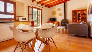 A modern kitchen with white appliances, a dining area with white chairs, a living room with a sofa, and a fireplace. - Country House 'Sa Caseta' with Mountain View, Private Pool and Wi-Fi (Artà)
