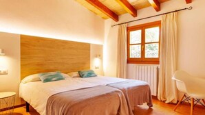 A double bed with two pillows, a bedside table, a window with curtains, and a chair. - Country House 'Sa Caseta' with Mountain View, Private Pool and Wi-Fi (Artà)