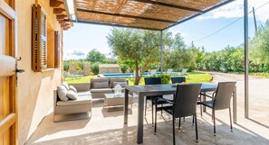 Un patio exterior con una mesa y sillas, un sofá, y vistas a una piscina y vegetación.