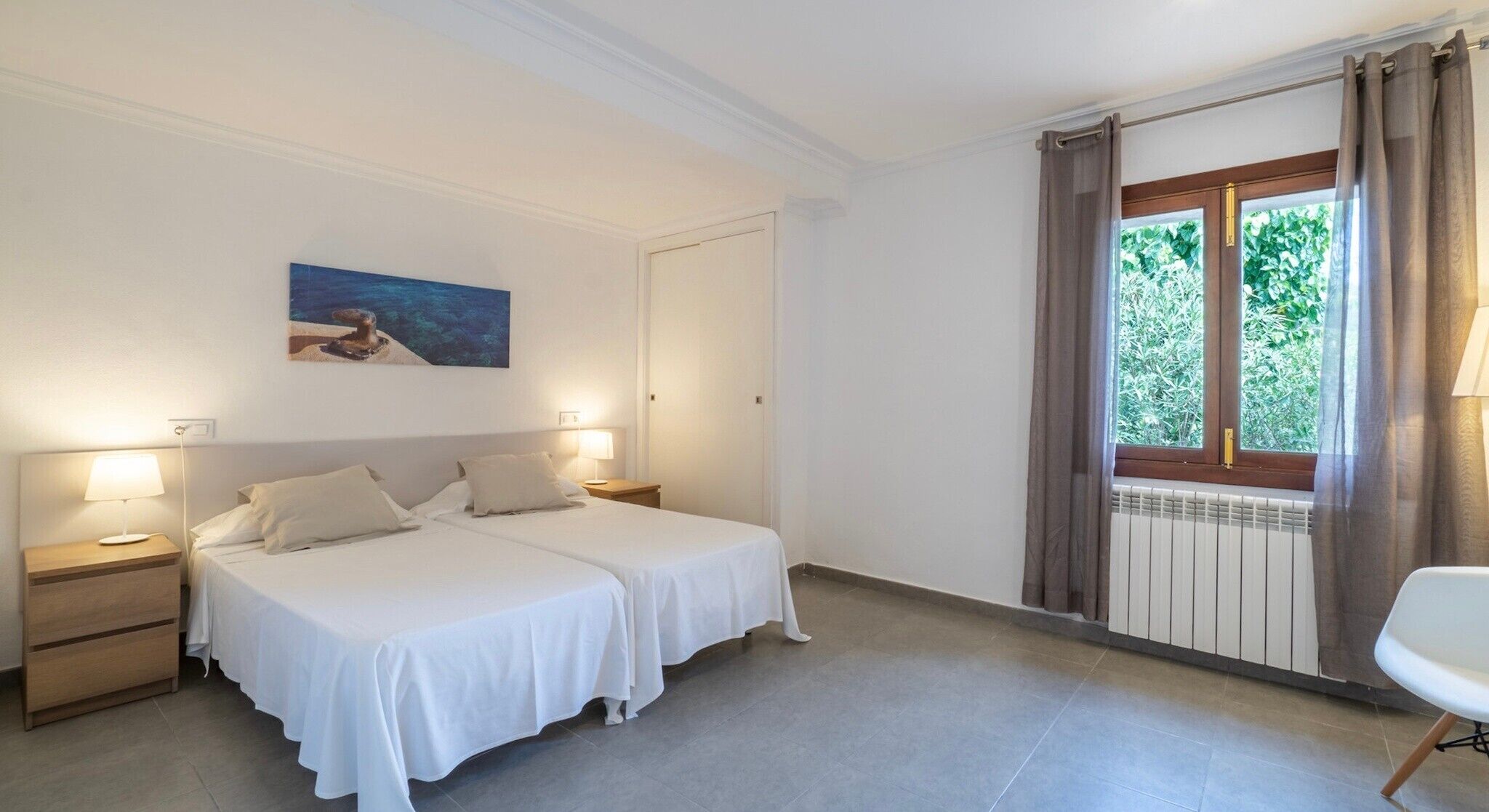 Ein Hotelzimmer mit zwei Betten, einem fensterbelaubten Fenster, einem Bild an der Wand und einem Sessel.