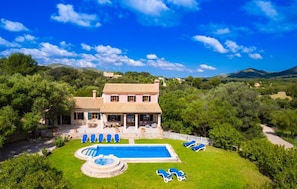 Una villa con piscina, múltiples sillas de descanso y un jardín bien cuidado.