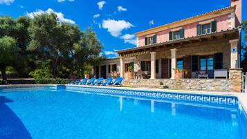 A pool with blue tiles, a stone building with columns, and a clear blue sky.