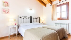 A double room with two beds, a wooden ceiling, a window with curtains, and a radiator. - Country House 'Es Corto' with Mountain View, Private Pool and Wi-Fi (Illes Balears)