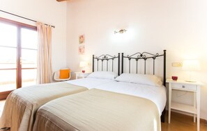 Ein Doppelbett mit Metallgestell, ein Nachttisch mit Lampe und ein Sessel mit orangenem Kissen.