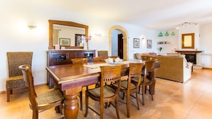 A dining area with a wooden table and chairs, a fireplace, and a kitchen in the background. - Country House 'Es Corto' with Mountain View, Private Pool and Wi-Fi (Illes Balears)