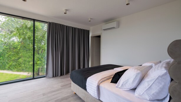 A modern bedroom with a large bed, a view of greenery through floor-to-ceiling windows, and an air conditioning unit on the wall. - Willkommen in der Villa Nene, Ihrem Traumurlaubsparadies (Pićan)