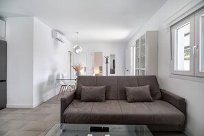 Un salon moderne avec un canapé, une table basse en verre et un coin cuisine à l’arrière-plan.