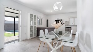 A modern kitchen with white cabinets, a dining area with a glass table and white chairs, and a view of a swimming pool.
