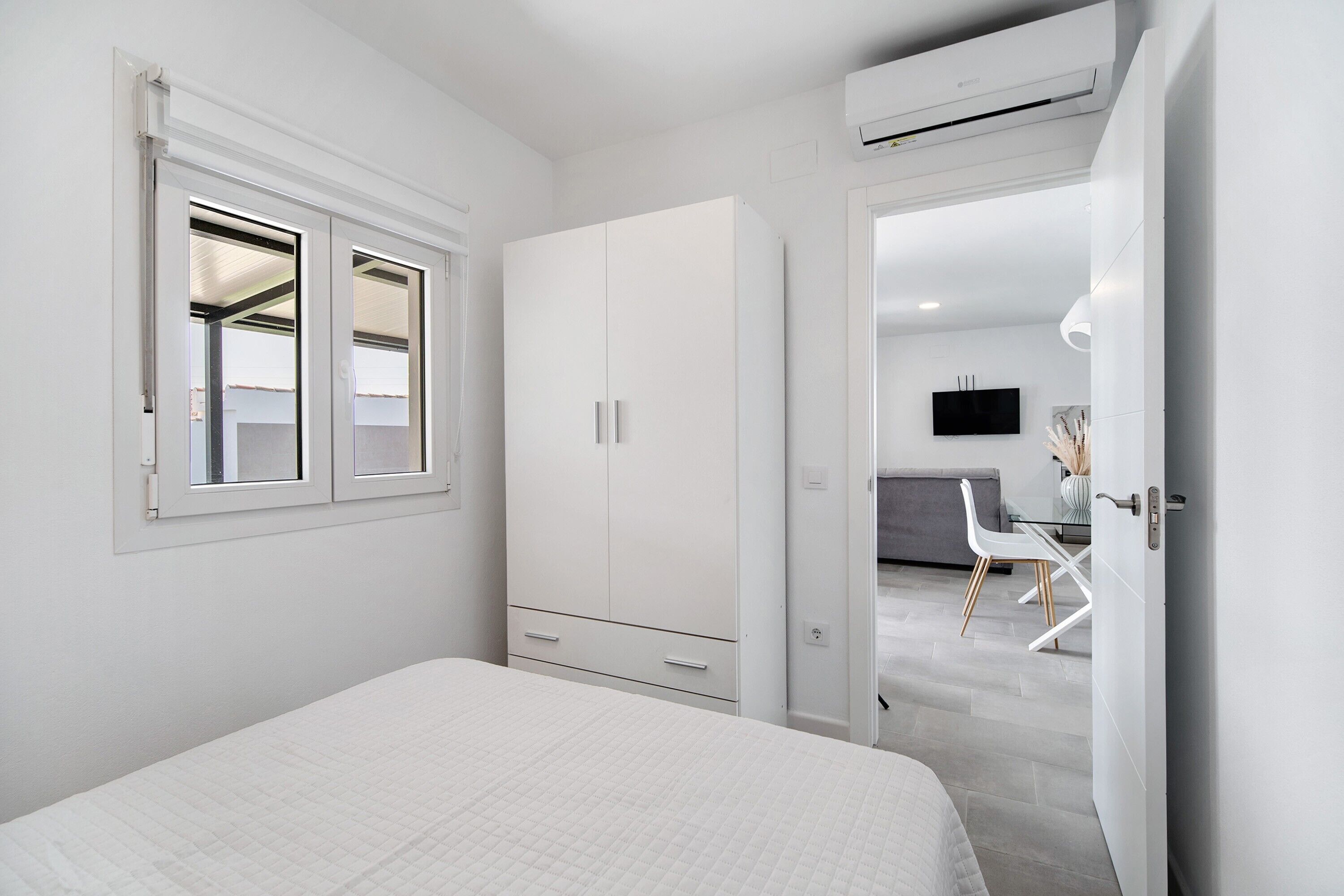 A bedroom with a bed, a wardrobe, a desk with a chair, and a television on the wall.