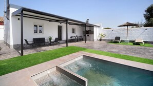 A modern outdoor pool area with a covered patio, seating, and a well-maintained lawn.