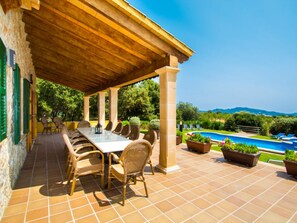 Patio esterno con un tavolo lungo e sedie, piscina e vista sulle colline.