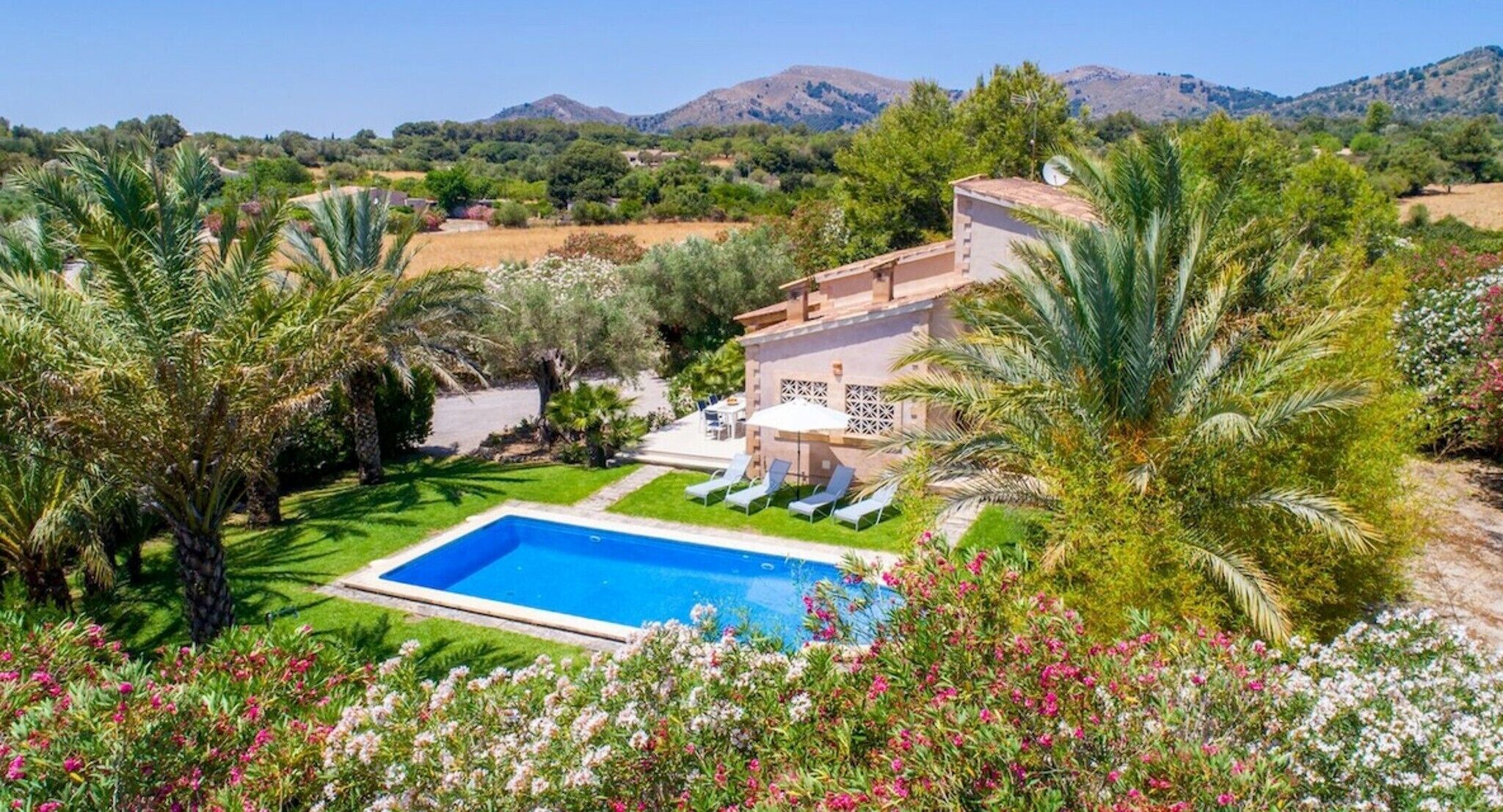 Una piscina con vistas a montañas, una casa con terraza y abundante vegetación.