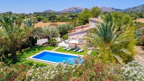 Une piscine avec vue sur les montagnes, une maison dotée d’une terrasse et une végétation luxuriante.
