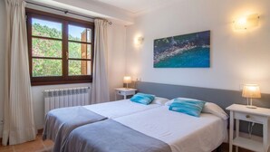 Une chambre à coucher avec un lit, deux tables de chevet, une fenêtre avec des rideaux, un radiateur et un tableau au mur.