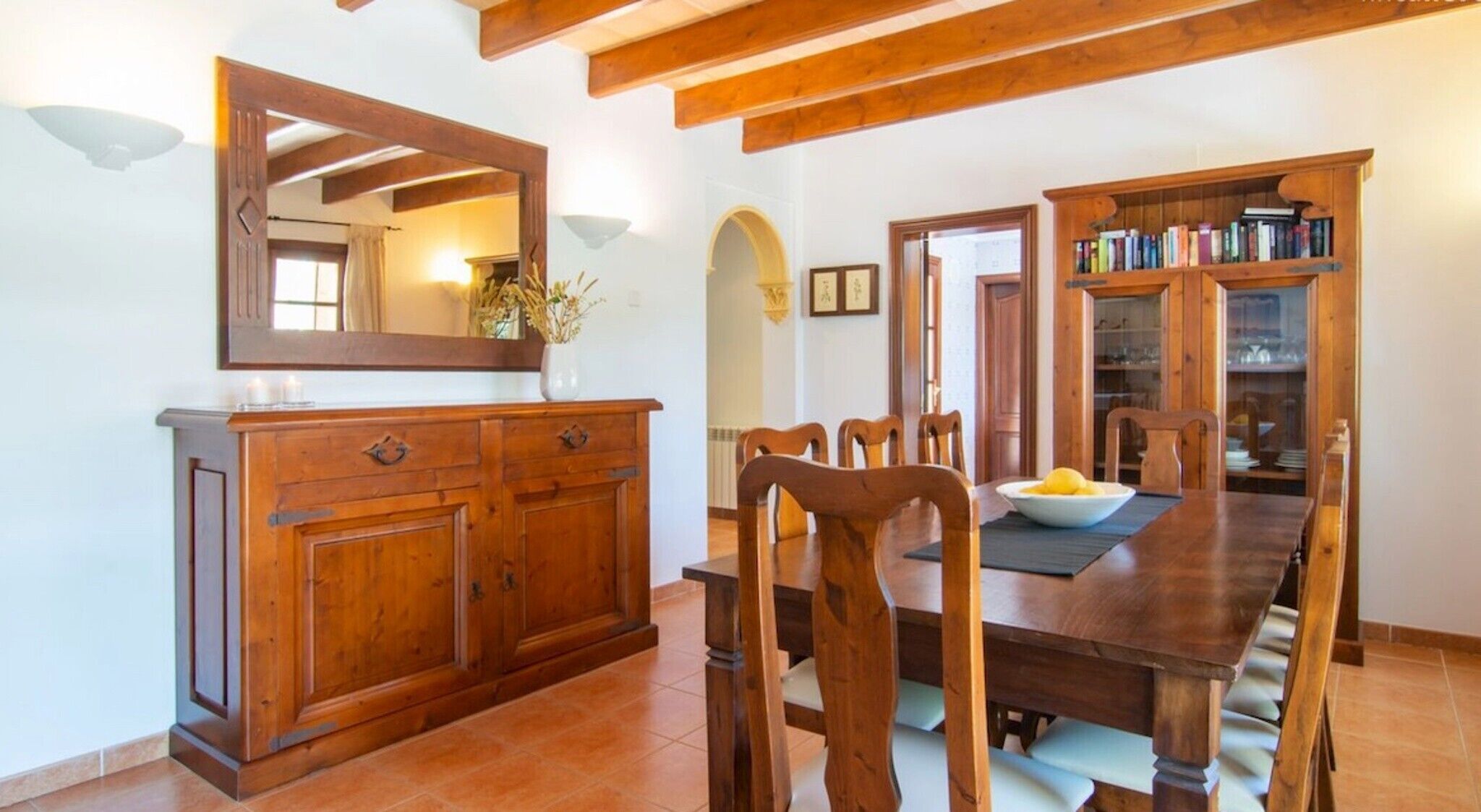 Un comedor con una mesa de madera, sillas, un armario y un espejo.