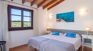 A bedroom with two beds, a window with curtains, a painting on the wall, and bedside lamps.