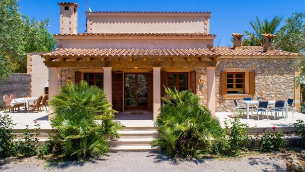 Une maison en pierre à deux étages, avec un toit en tuiles, une entrée centrale et des espaces extérieurs aménagés pour se détendre.