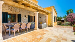 Un patio exterior techado con pared de piedra, una parrilla y mobiliario de mimbre.