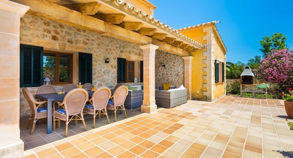 Une terrasse extérieure couverte, dotée d’un mur en pierre, d’un barbecue et de mobilier en osier.