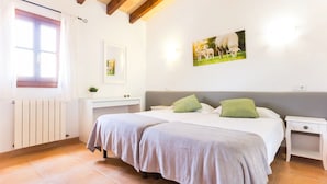 Un dormitorio con una cama doble, dos mesitas de noche, un radiador, una ventana con cortinas y un cuadro colgado en la pared.