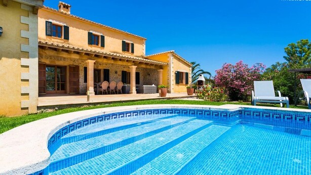 Una casa de dos pisos con piscina, muebles de jardín y un jardín con flores rosas.