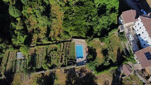 Vista aérea de uma propriedade com piscina, jardim em terraços e edifícios residenciais próximos.