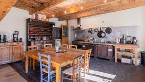 A rustic kitchen with wooden beams, a central dining table, and various kitchen appliances. - Room 'La Ferme De Chalas - Dénave' with Shared Pool, Shared Terrace and Wi-Fi (Valgorge)