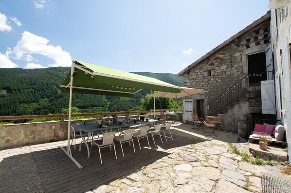 An outdoor patio with a table and chairs, a stone floor, and a view of a forested mountain.
