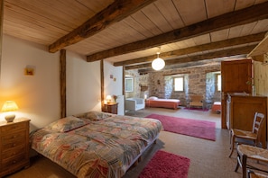 Una camera da letto con un letto, travi in legno, una parete in pietra, una scrivania e una sedia.