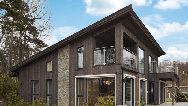 Ett modernt hus i två våningar med en fasad av sten, stora fönster och en balkong.