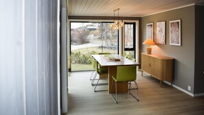 Ett modernt matområde med ett träbord, gröna stolar och utsikt genom stora fönster mot en trädgård.
