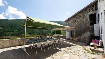 An outdoor patio with a table and chairs, a stone floor, and a view of a forested mountain.