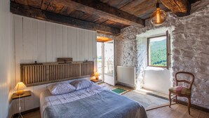 Een slaapkamer met een houten hoofdeinde, een bed met een grijze deken, een hanglamp, een stoel en een stenen muur.