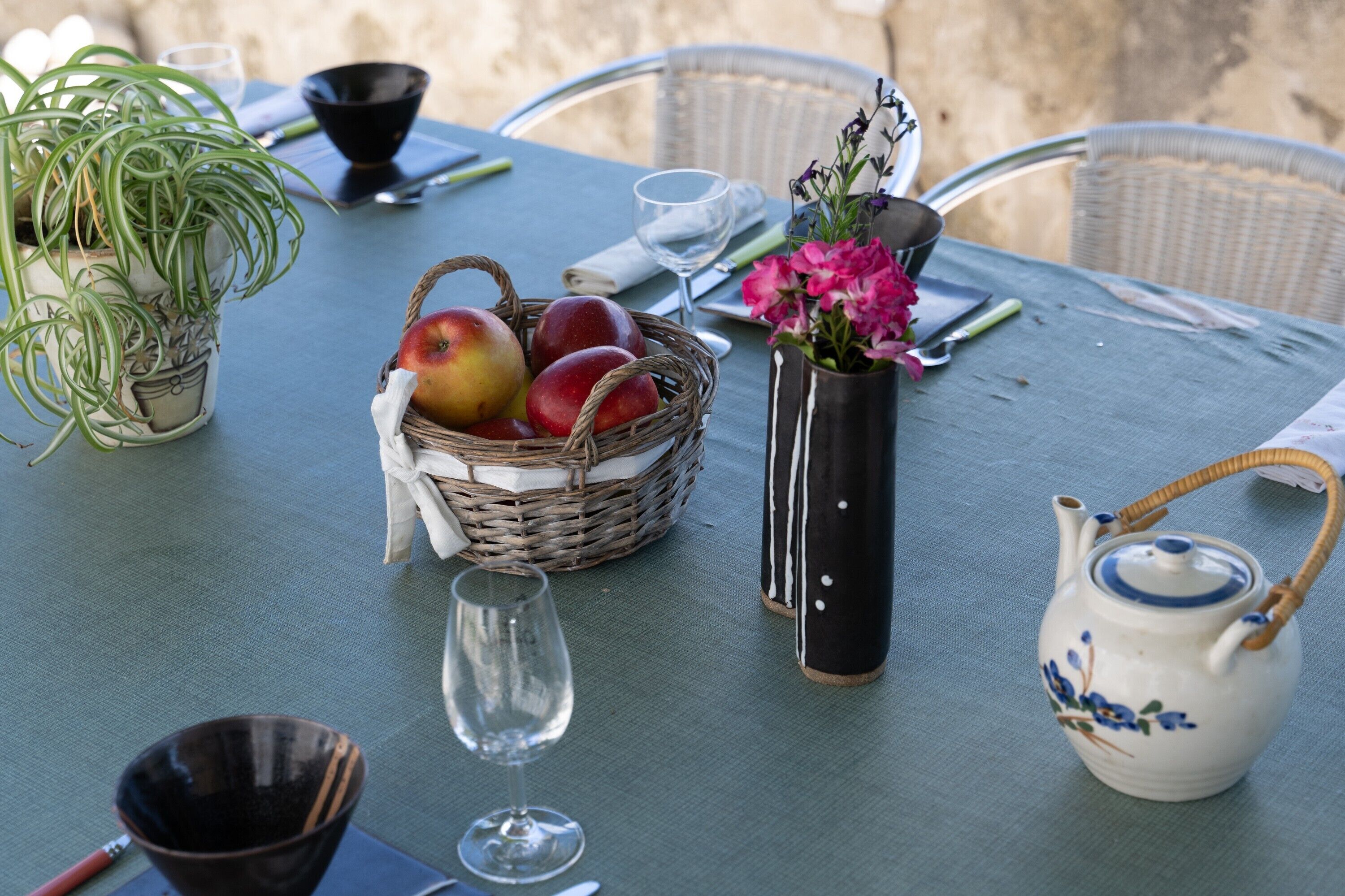 Una mesa servida con una cesta de fruta, un florero con flores, una tetera y un cuenco.