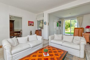 Sala de estar con dos sofás blancos, una mesa de centro con una planta y vistas al exterior a través de una puerta de cristal.