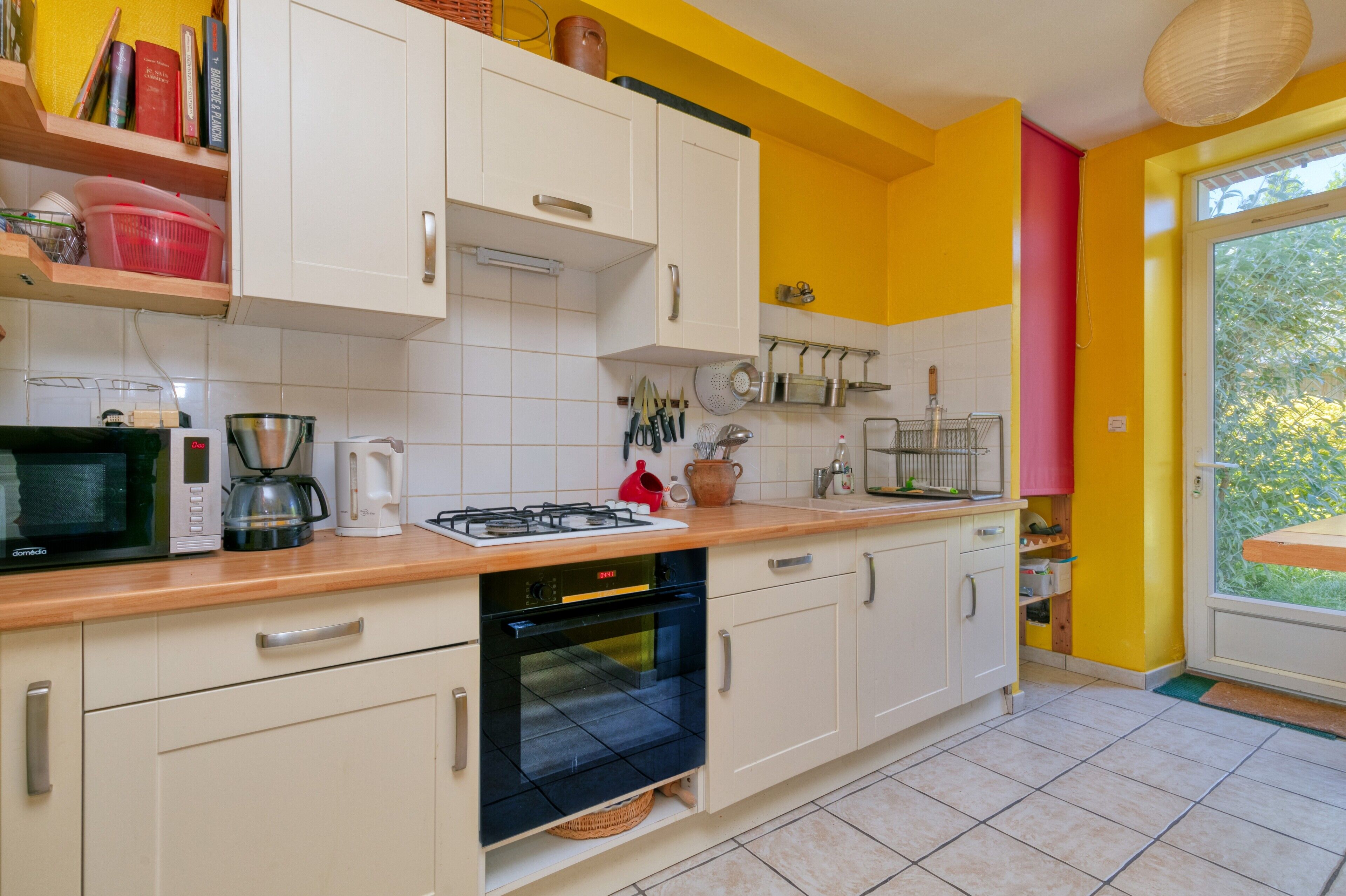 A kitchen with white cabinets, a microwave, a stove, and a window with a view of greenery.